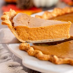 A slice of pumpkin pie being lifted from a pie plate with a spatula.
