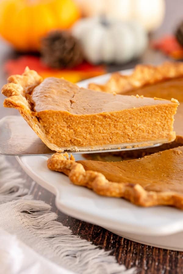 A slice of pumpkin pie being lifted from a pie plate with a spatula.