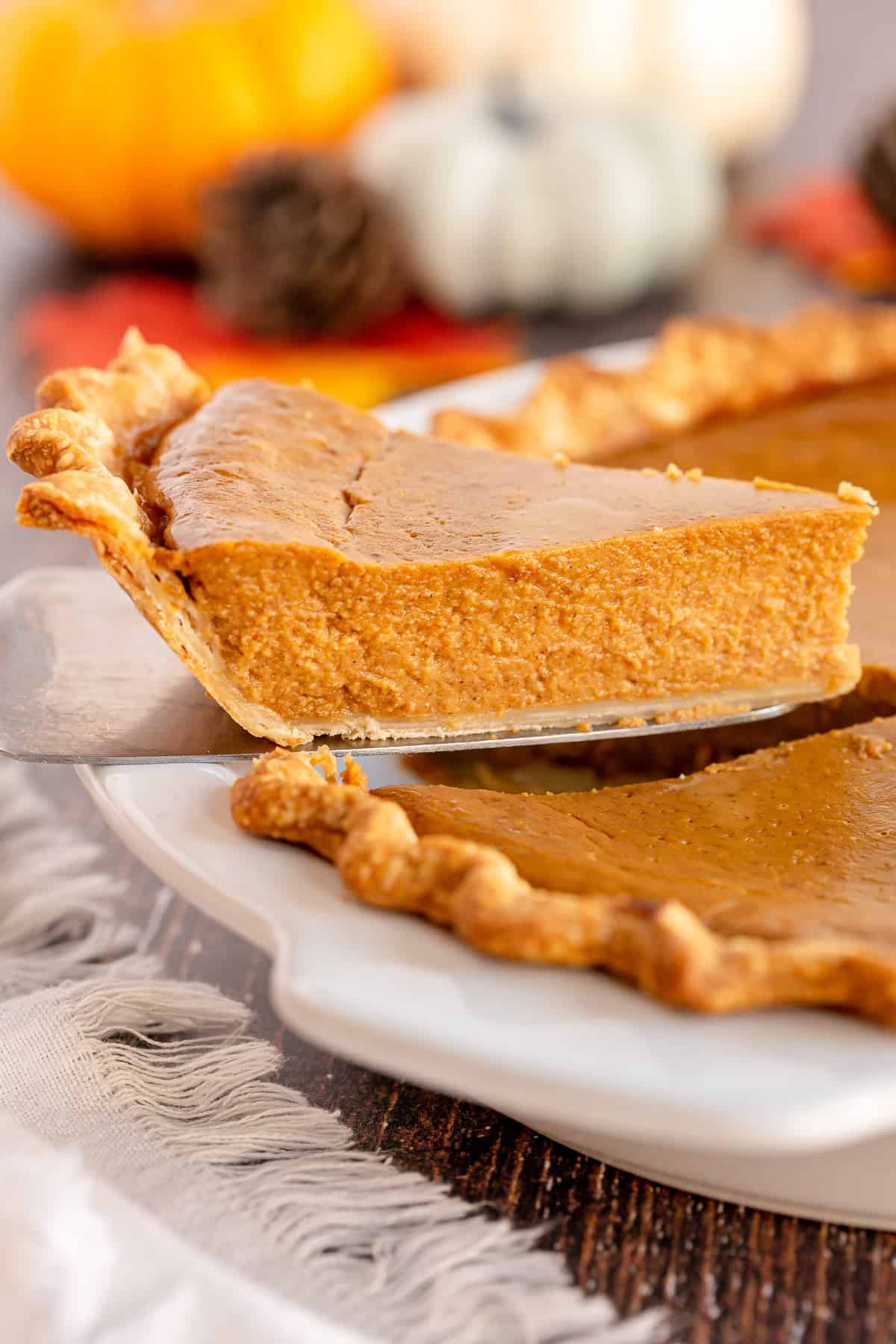 A slice of pumpkin pie being lifted from a pie plate with a spatula.