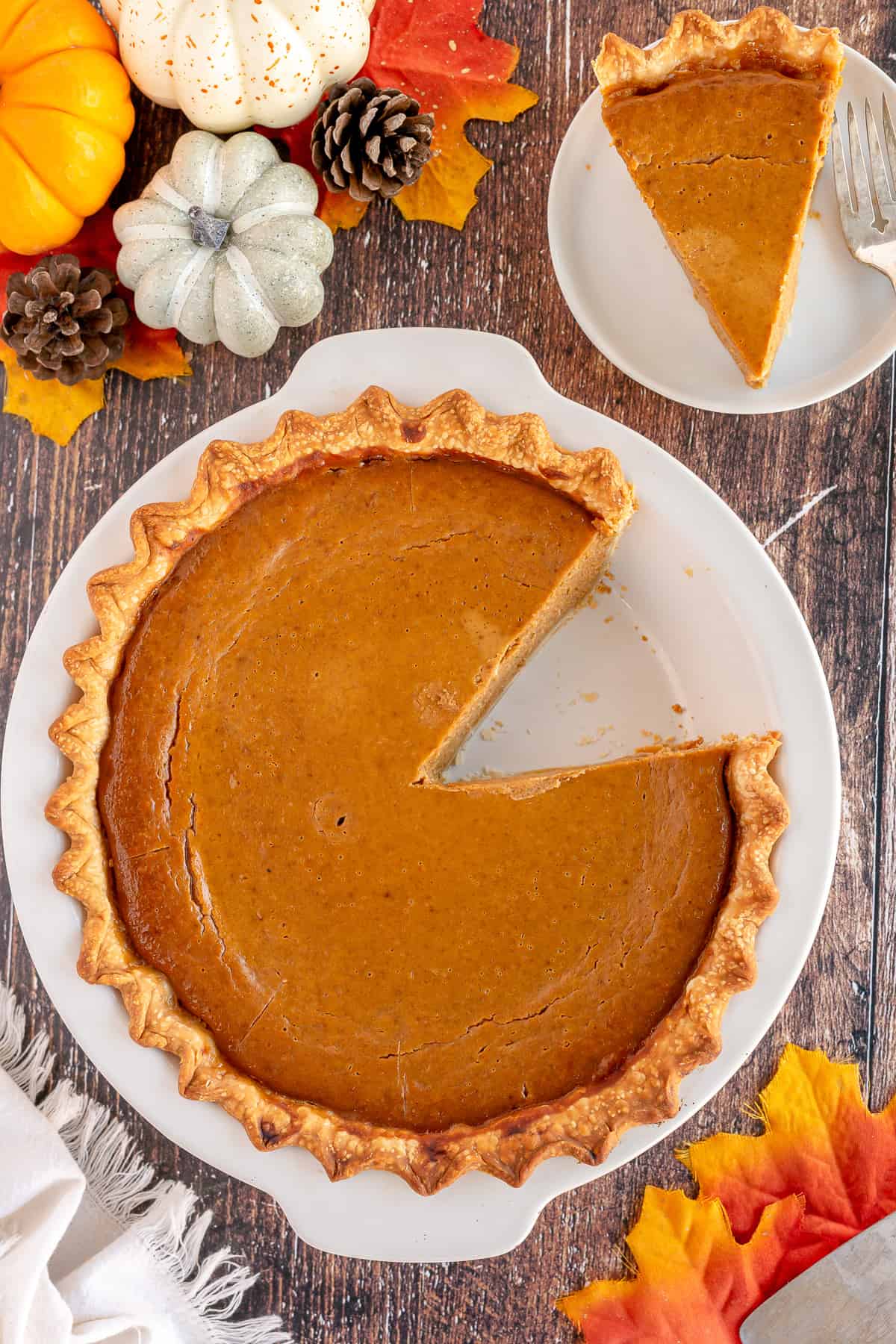 An over the top shot of a pumpkin pie with a slice missing next to a plate with a slice.