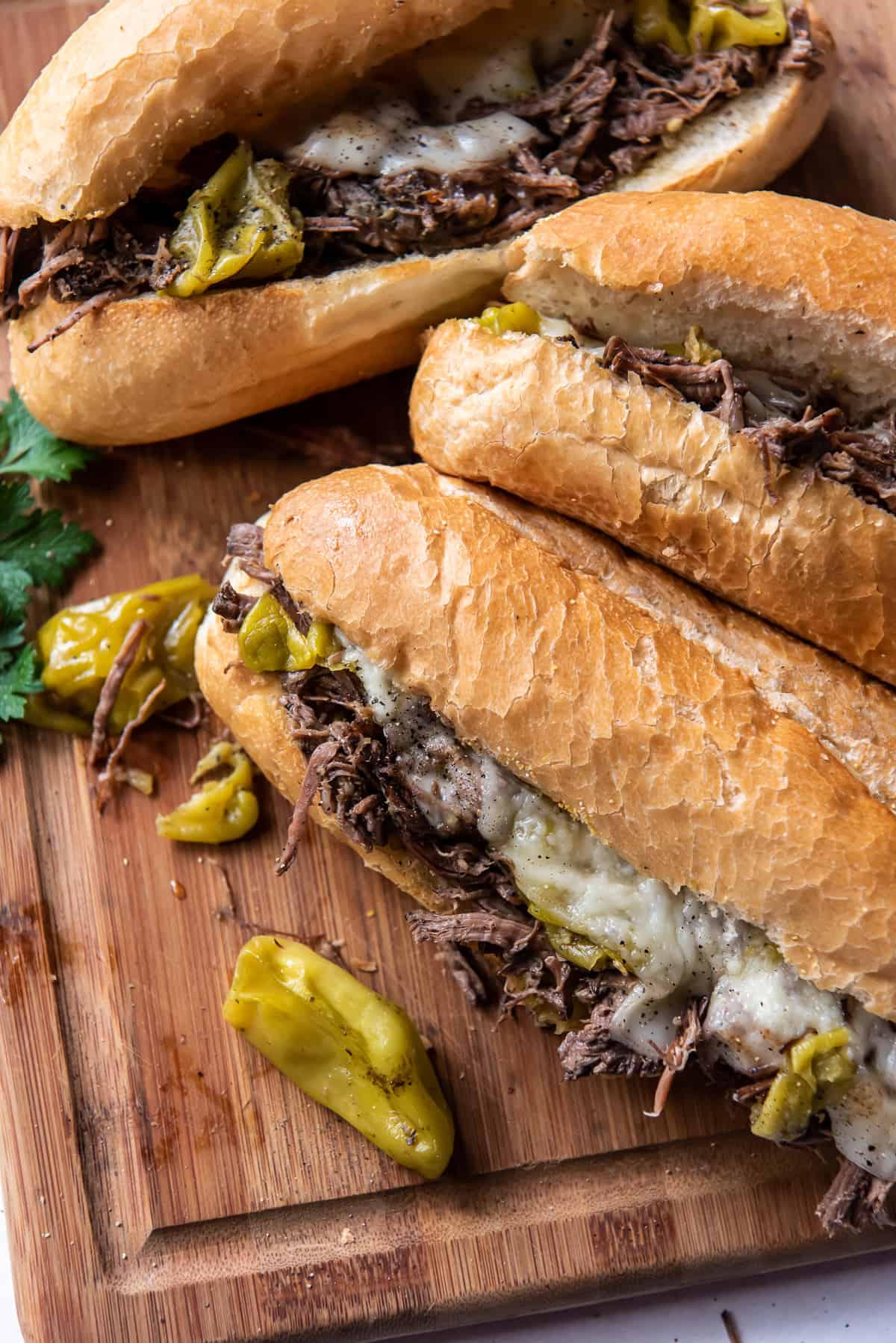 Italian Beef Sandwiches on rolls with melted provolone cheese and pepperoncini.