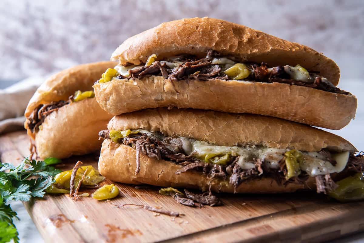 Three Italian Beef Sandwiches on a wood cutting board.