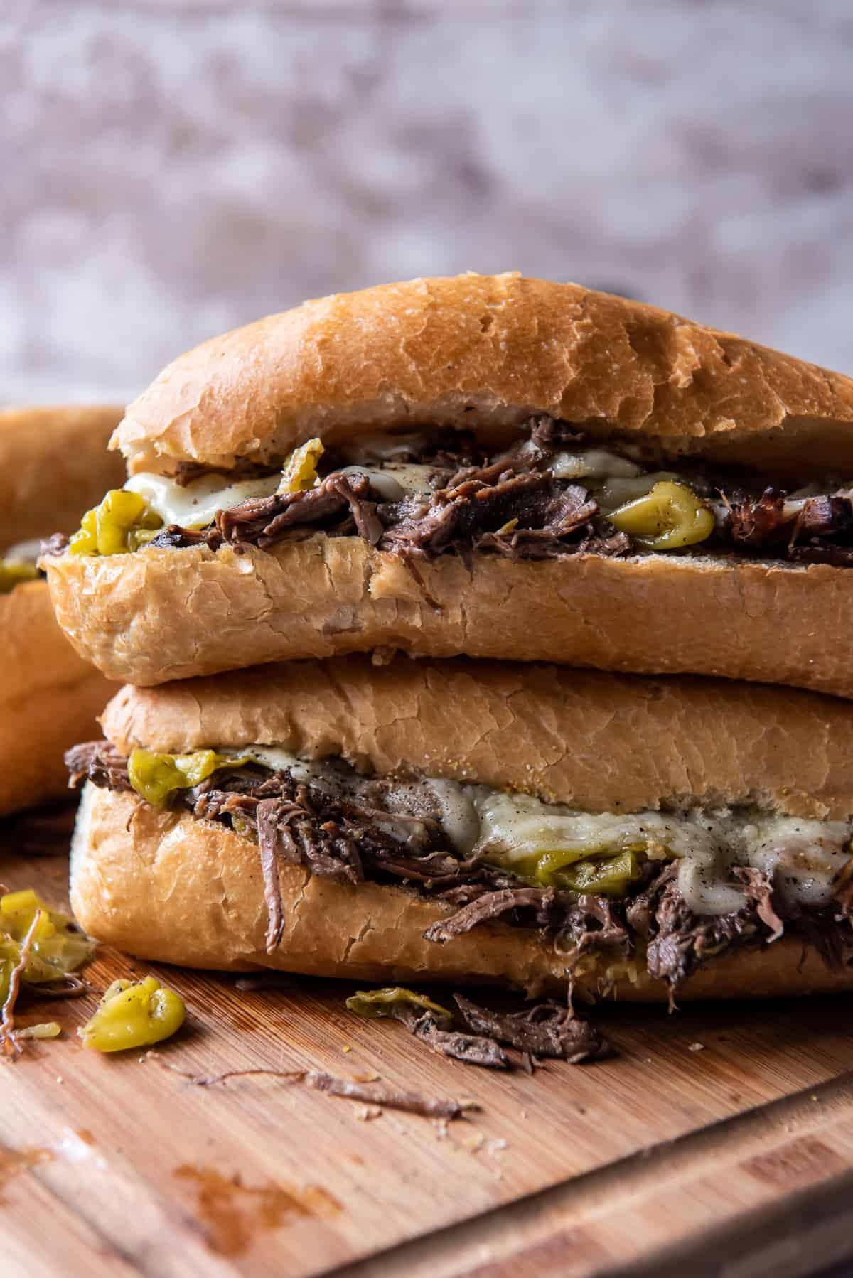 Two Italian Beef Sandwiches stacked on a cutting board.