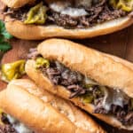 Three Italian Beef Sandwiches on a wood cutting board shot from over the top.