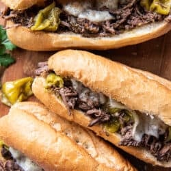 Three Italian Beef Sandwiches on a wood cutting board shot from over the top.