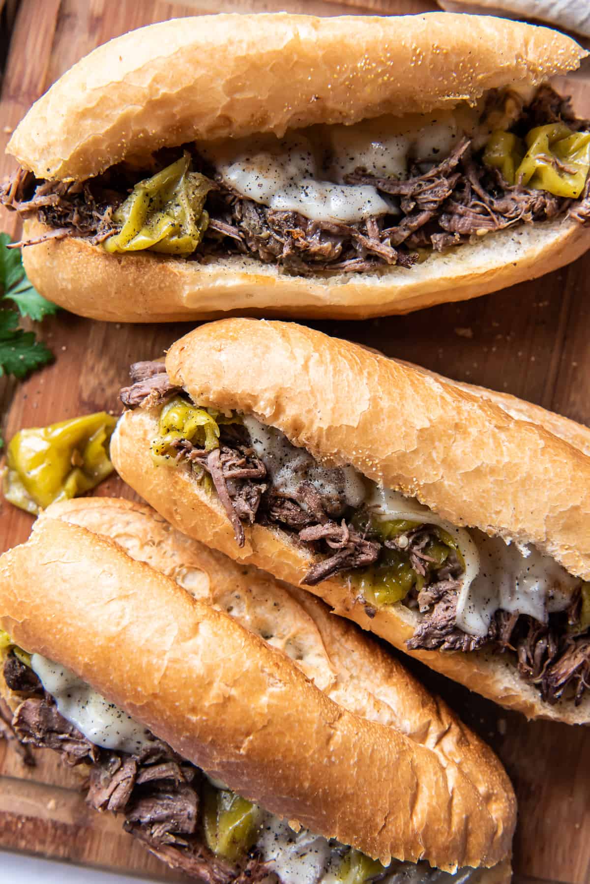 Three Italian Beef Sandwiches on a wood cutting board shot from over the top.