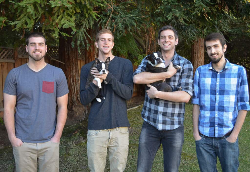Four young men lined up with two of holding Boston Terriers.