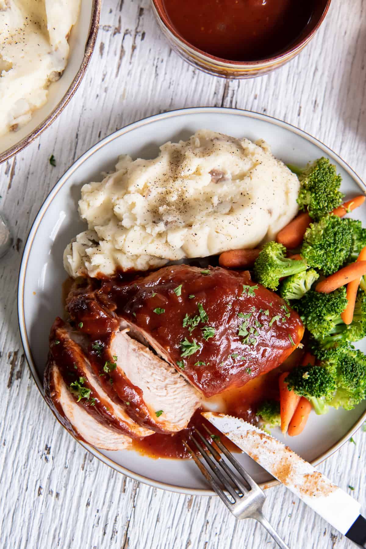 An over the top shot of sliced BBQ chicken on a plate with mashed potatoes and broccoli.