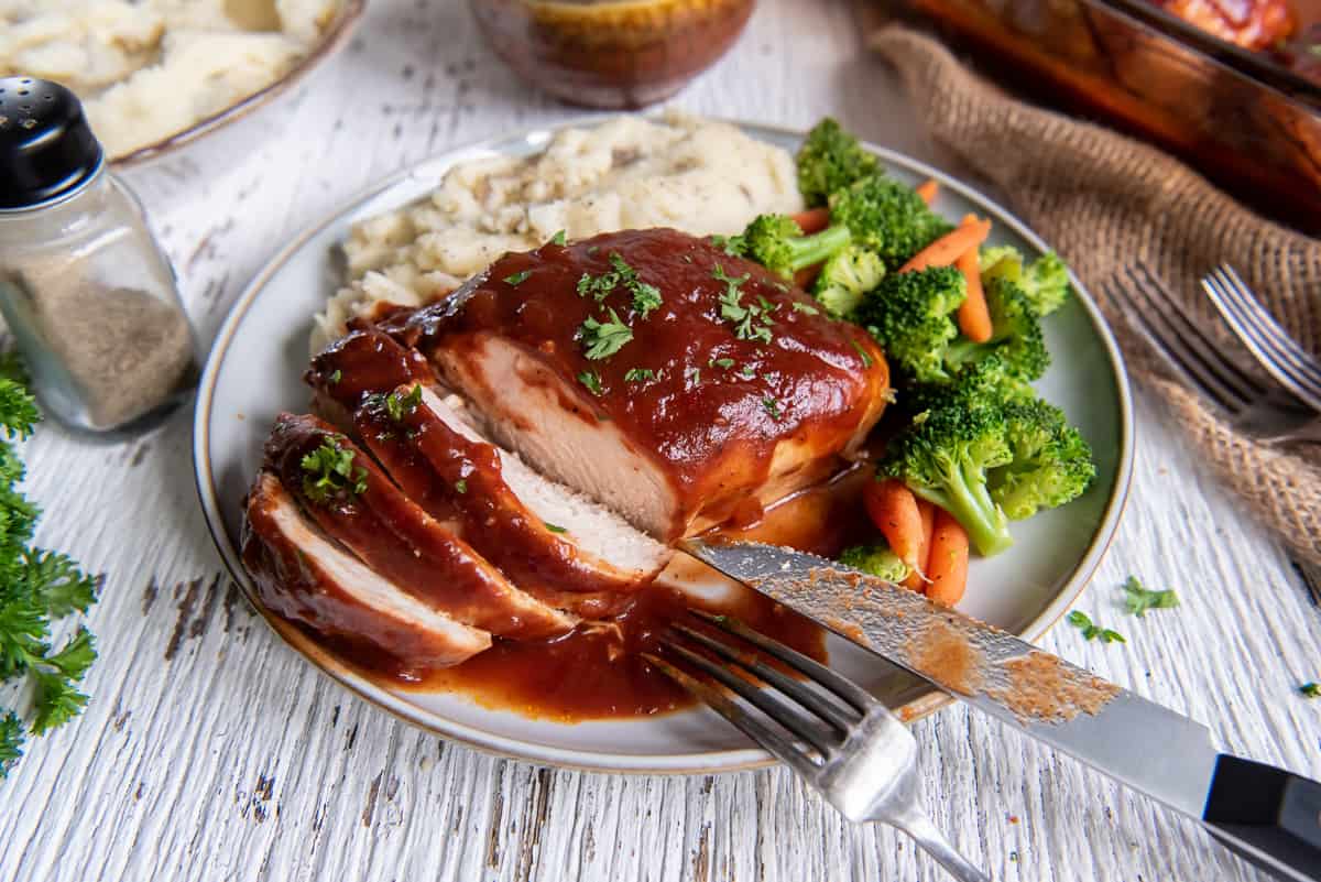 Sliced BBQ chicken on a plate with broccoli and mashed potatoes.