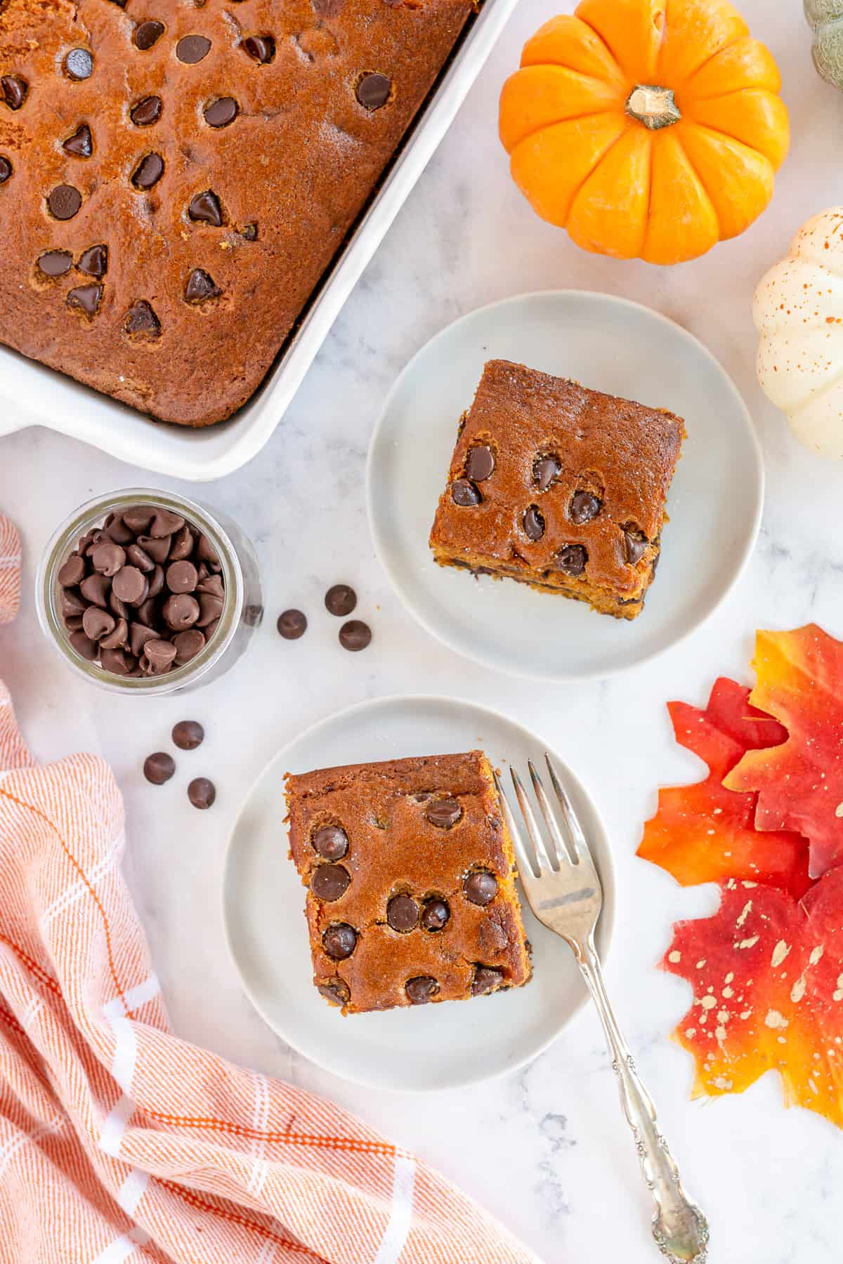 An over the top shot of a cake in a baking dish with two servings on plates next to it.