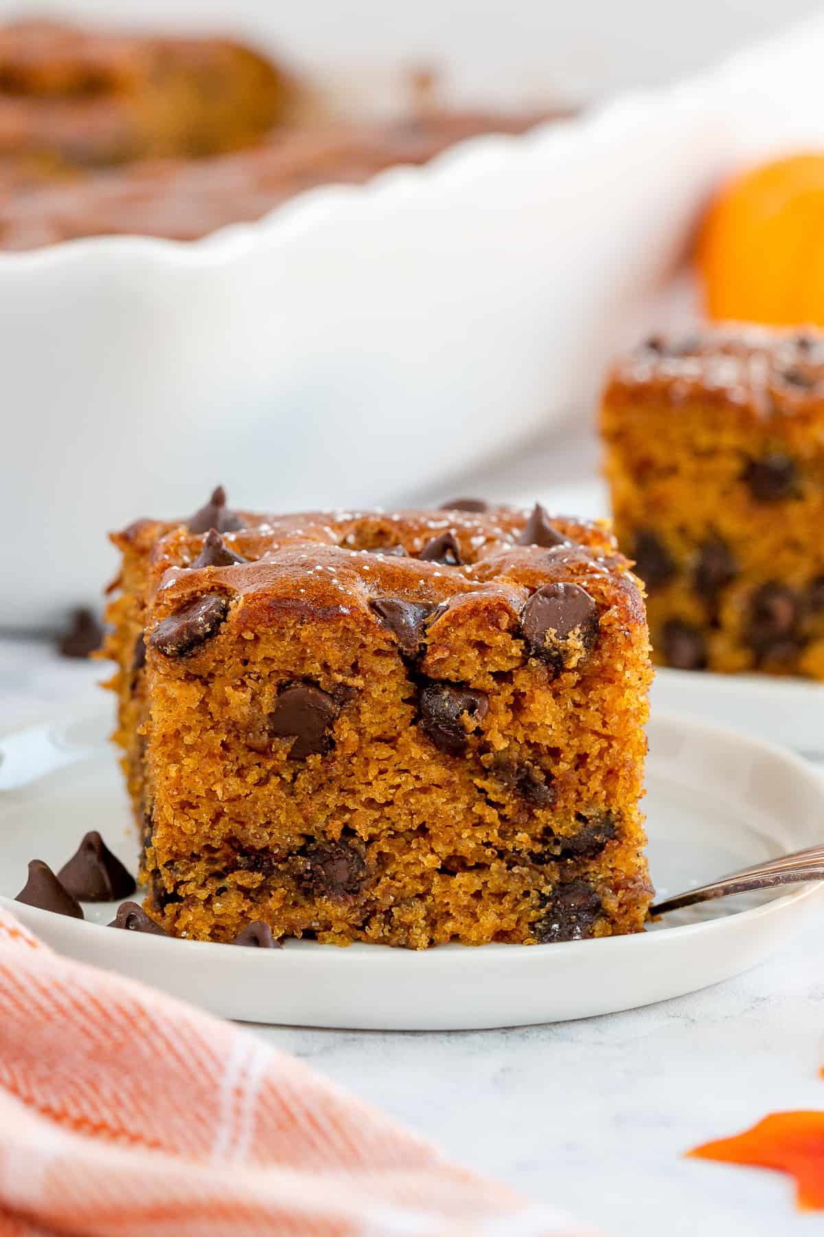 An eye level shot of a slice of Pumpkin Chocolate Chip Cake on a white plate.