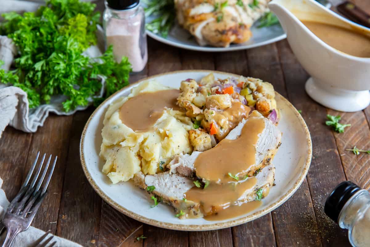 A plate with turkey, mashed potatoes and gravy in front of a gravy boat.