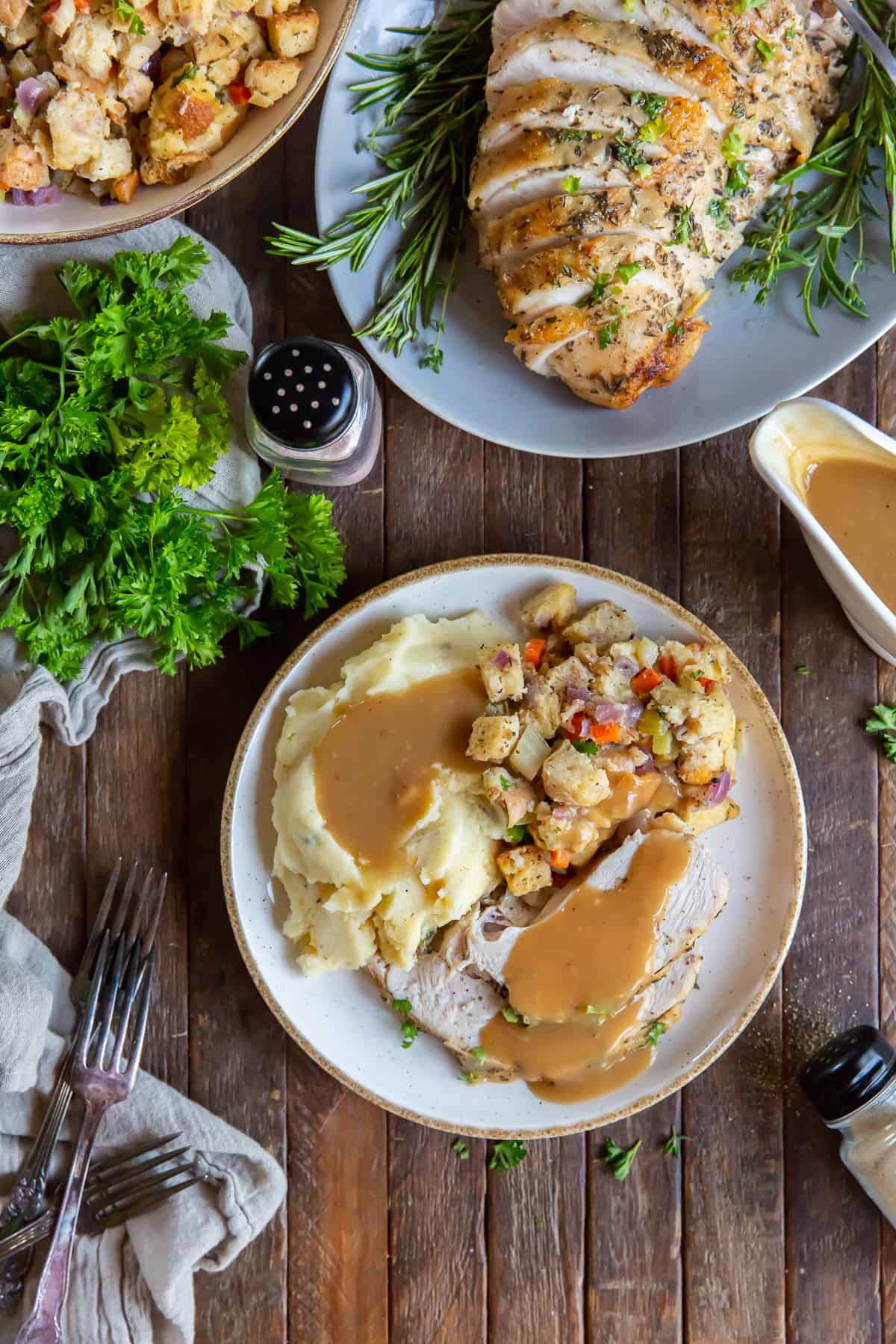 An over the top shot of a plate with turkey and gravy next to a bowl of stuffing and platter of turkey.