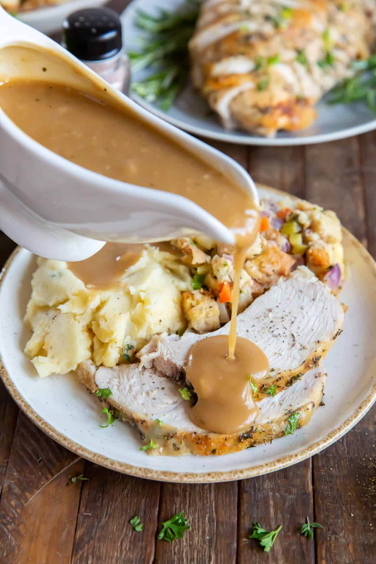 Gravy pouring from a gravy boat on to sliced turkey on a plate.