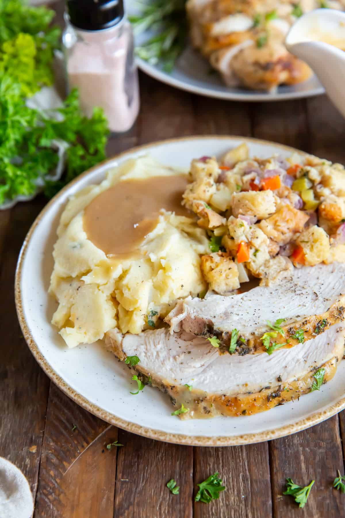 A dinner plate with sliced turkey, mashed potatoes and gravy, and stuffing on a dark board.