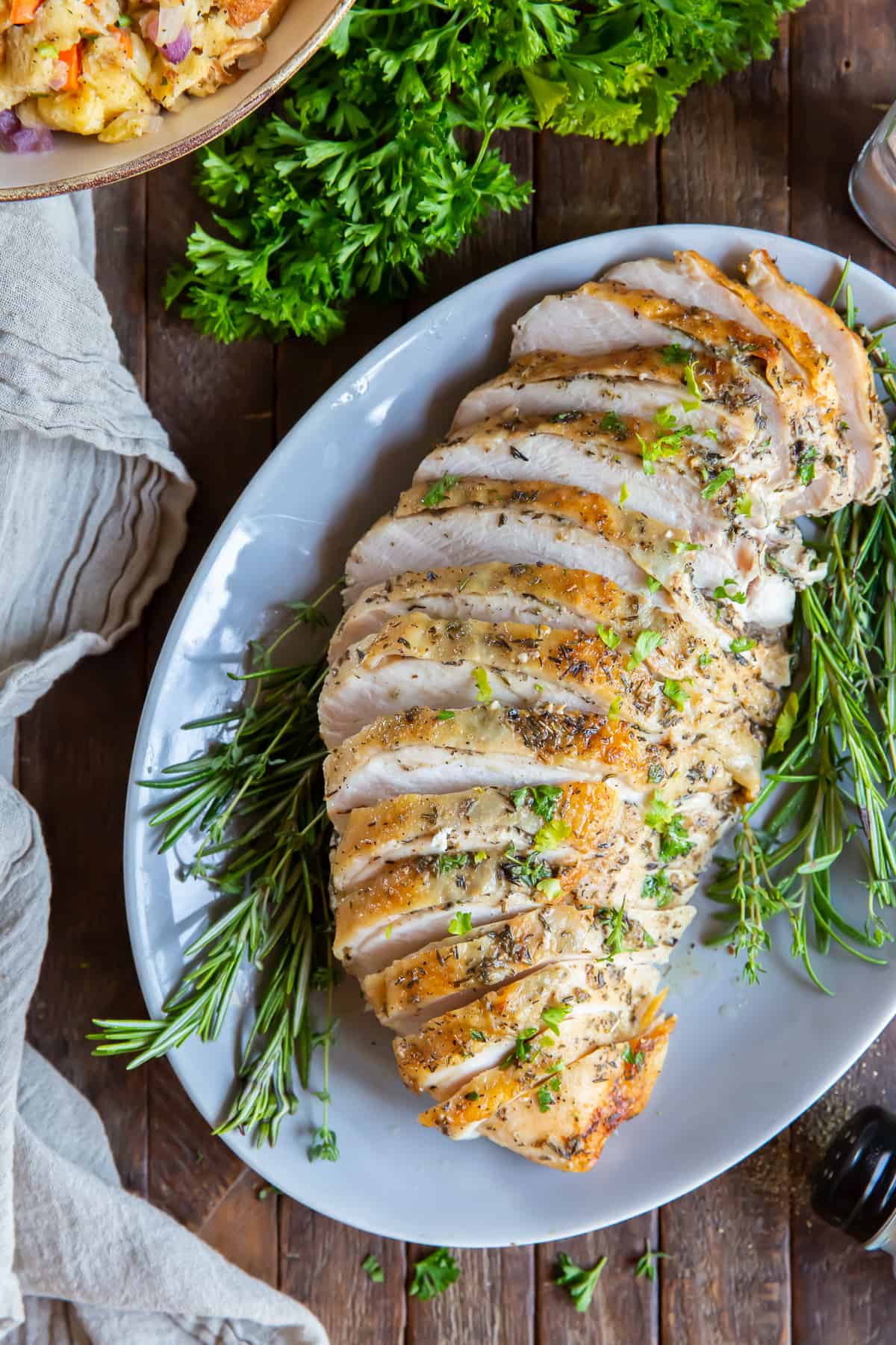 A sliced roasted turkey breast on a white platter with parsley.