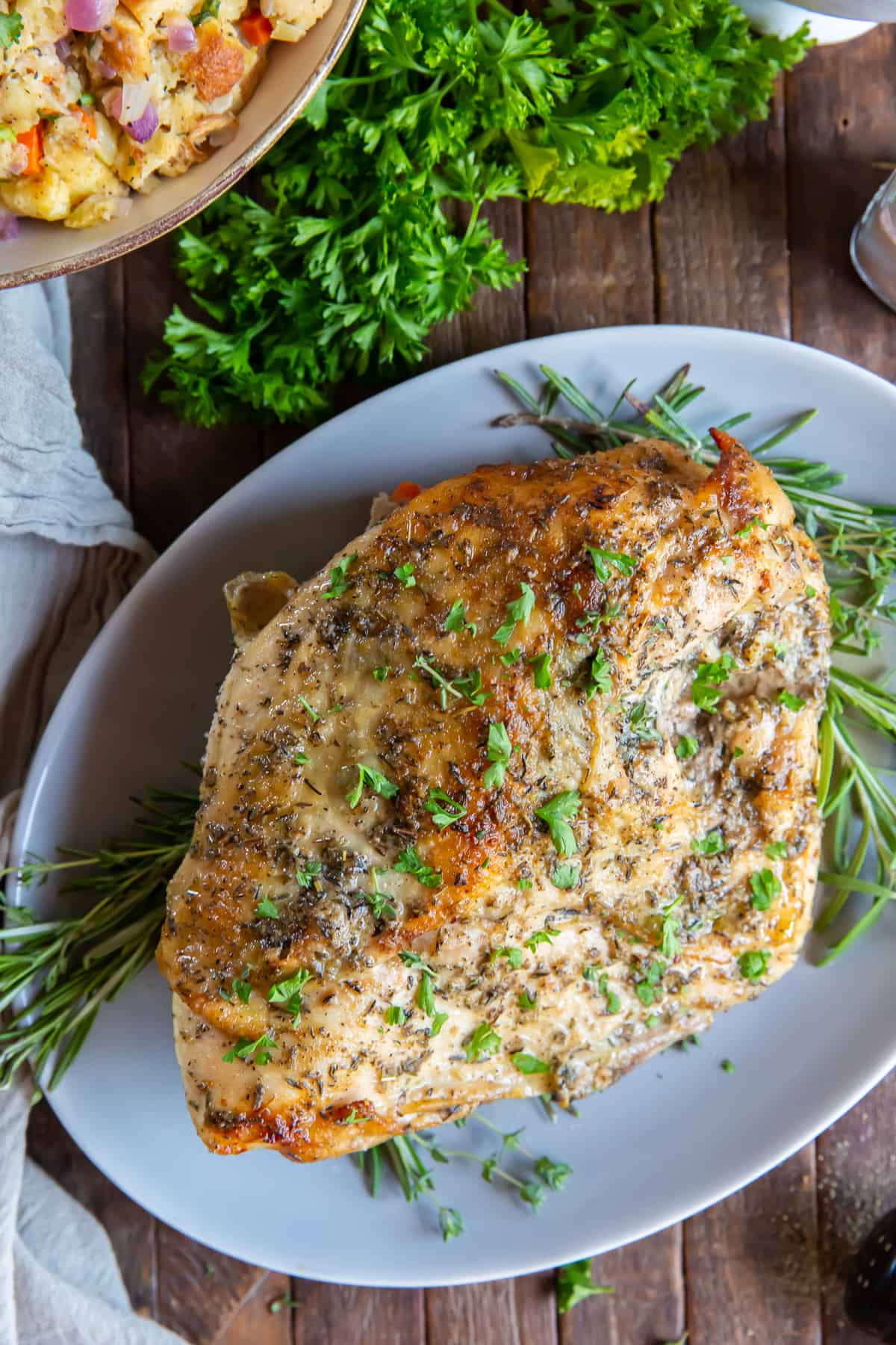 An over the top shot of a roasted turkey breast on a white platter with parsley.