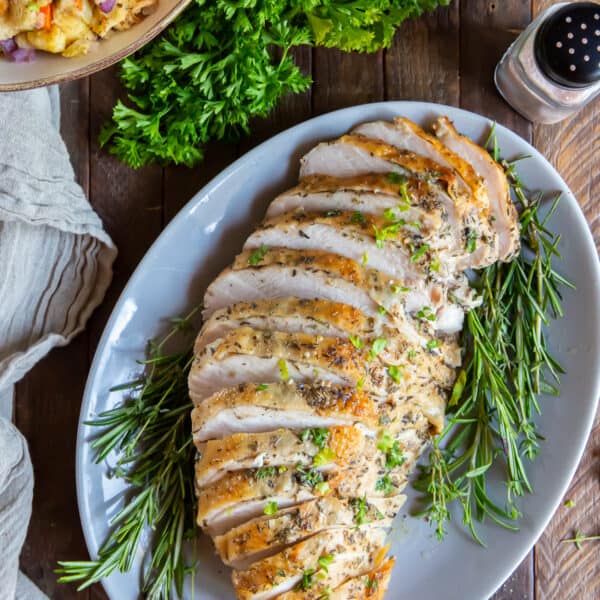 Sliced turkey breast on a white platter with rosemary.