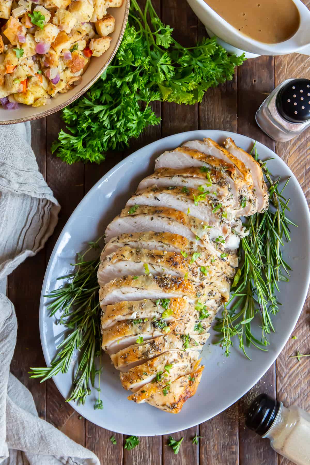 An over the top shot of sliced roasted turkey breast on a platter next to a gravy boat and bowl of stuffing.