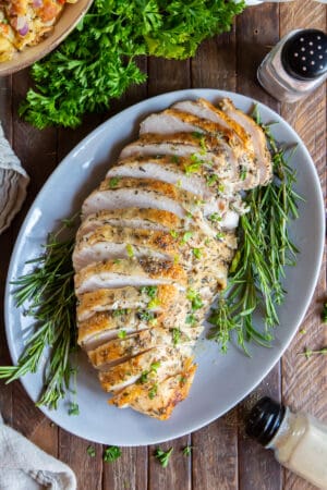 Sliced Roasted Turkey Breast on a white platter with fresh herbs.