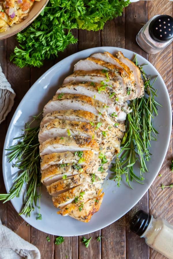 Sliced Roasted Turkey Breast on a white platter with fresh herbs.