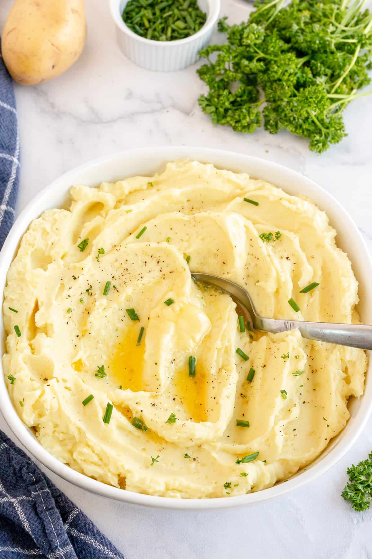 A white bowl filled with Sour Cream Mashed Potatoes with butter and chives.