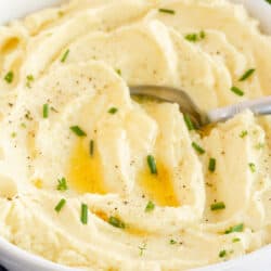 A white bowl filled with mashed potatoes topped with melted butter.