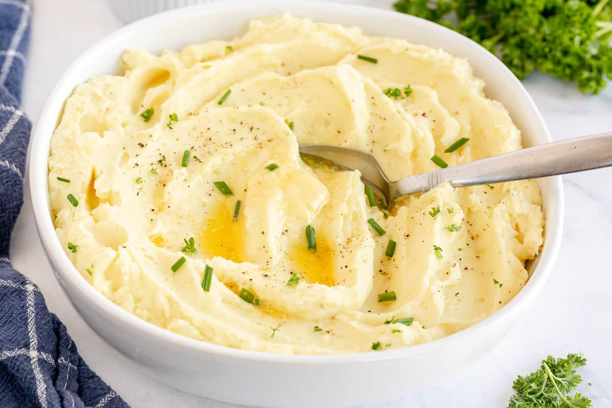 A white bowl filled with mashed potatoes topped with melted butter and chives.
