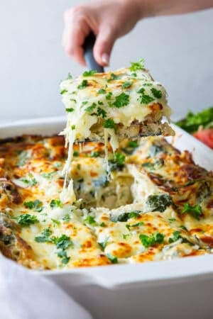 A spatula lifting a piece of lasagna from a baking dish.