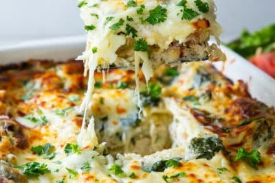 A spatula lifting a piece of lasagna from a baking dish.