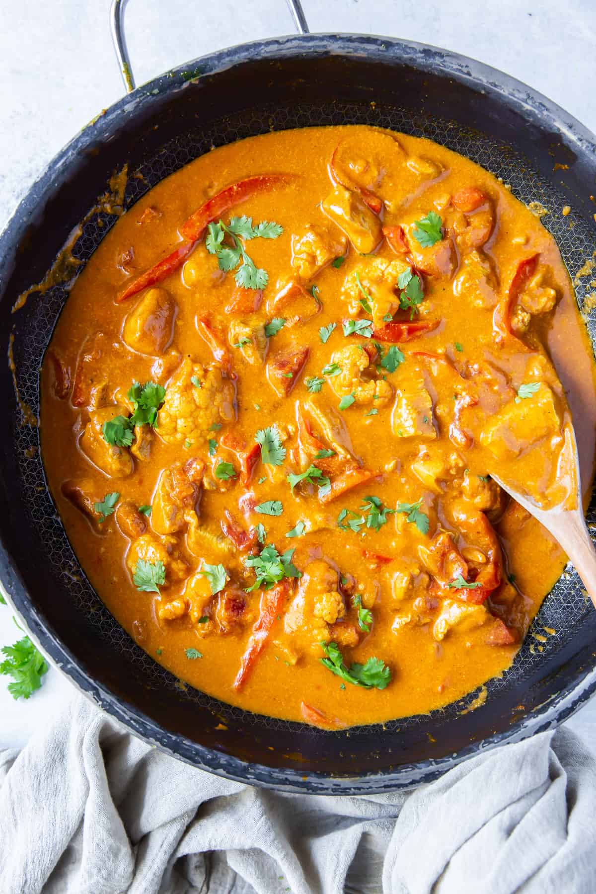 An over the top shot of curry chicken in a skillet with a wooden spoon.