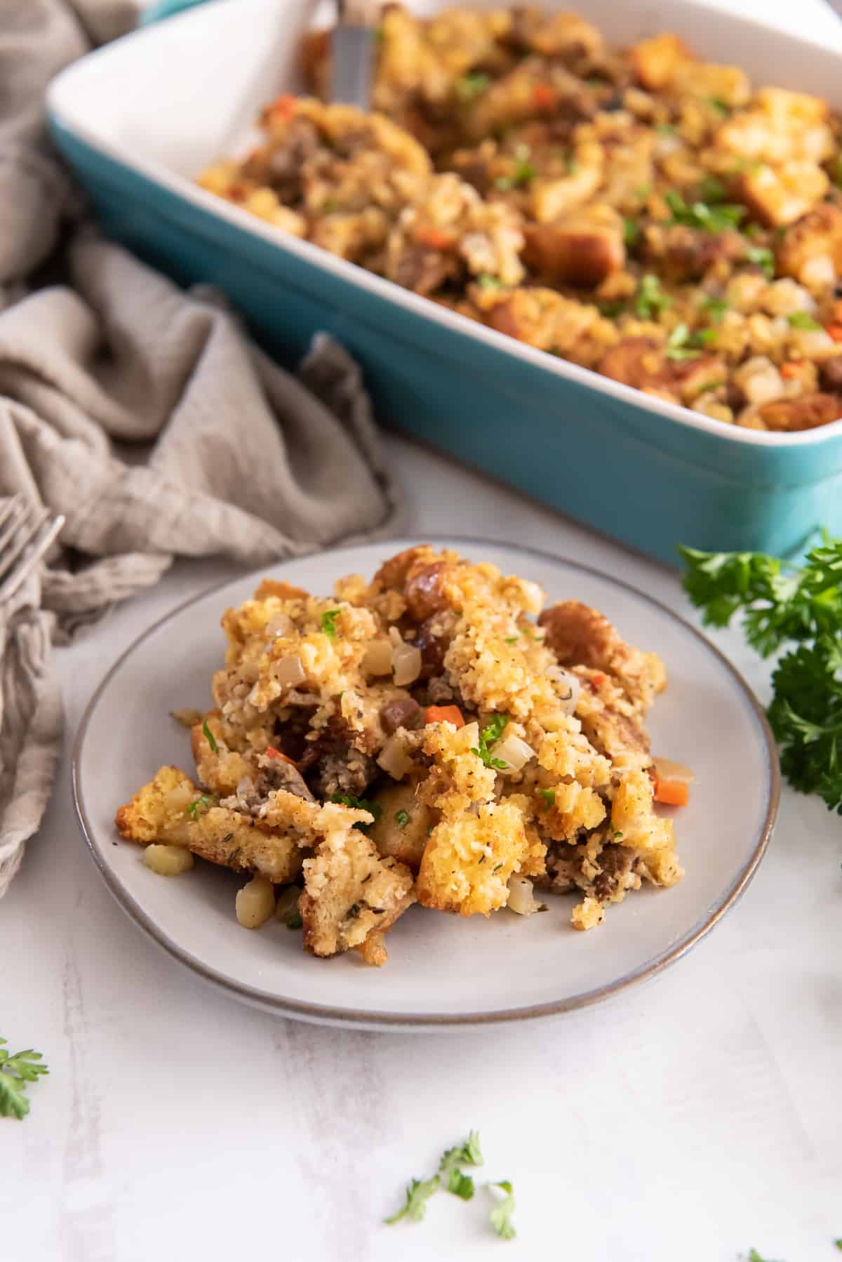A serving of stuffing on a small white plate in front of a blue casserole dish.