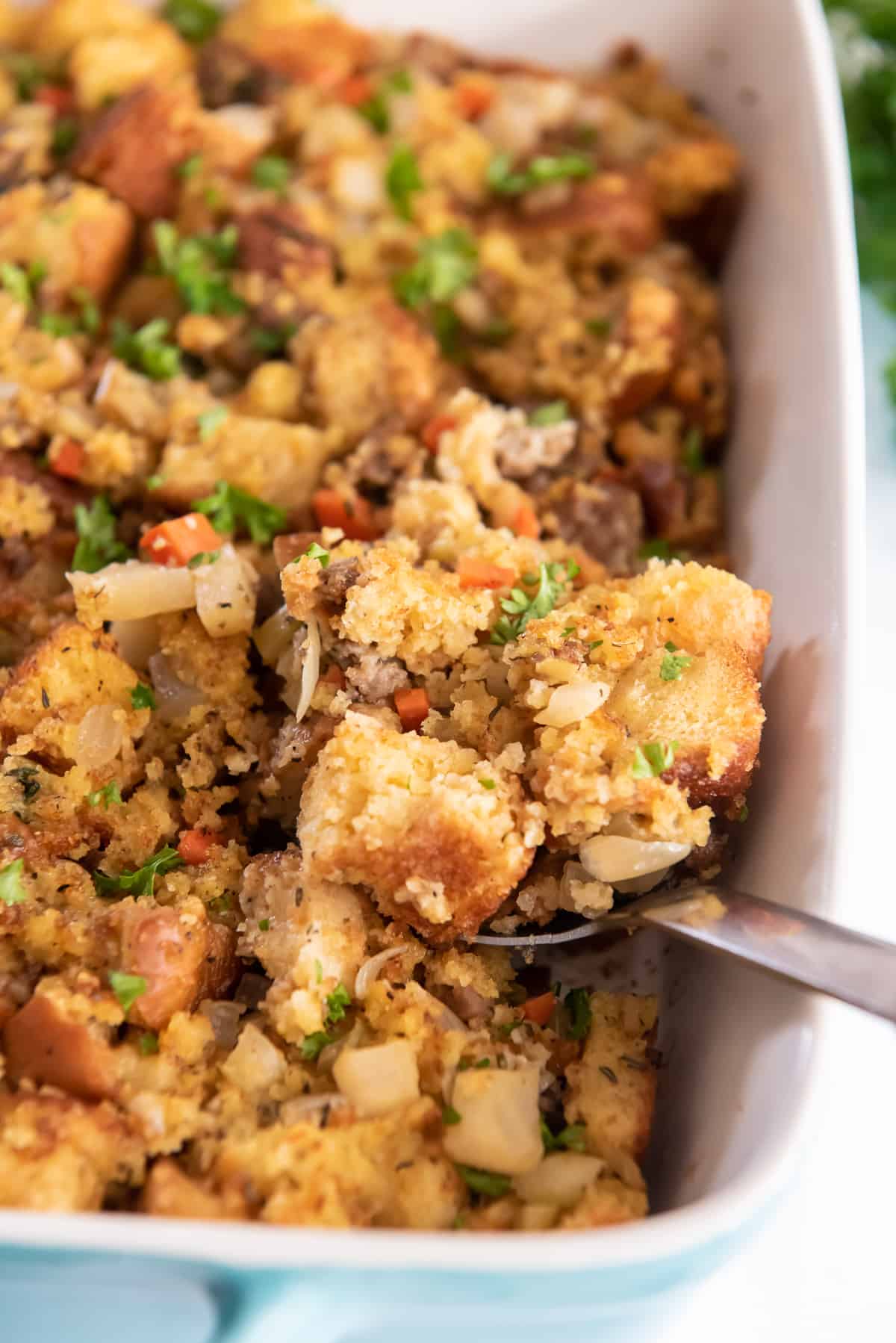 A spoon scooping up Jiffy cornbread stuffing from a baking dish.