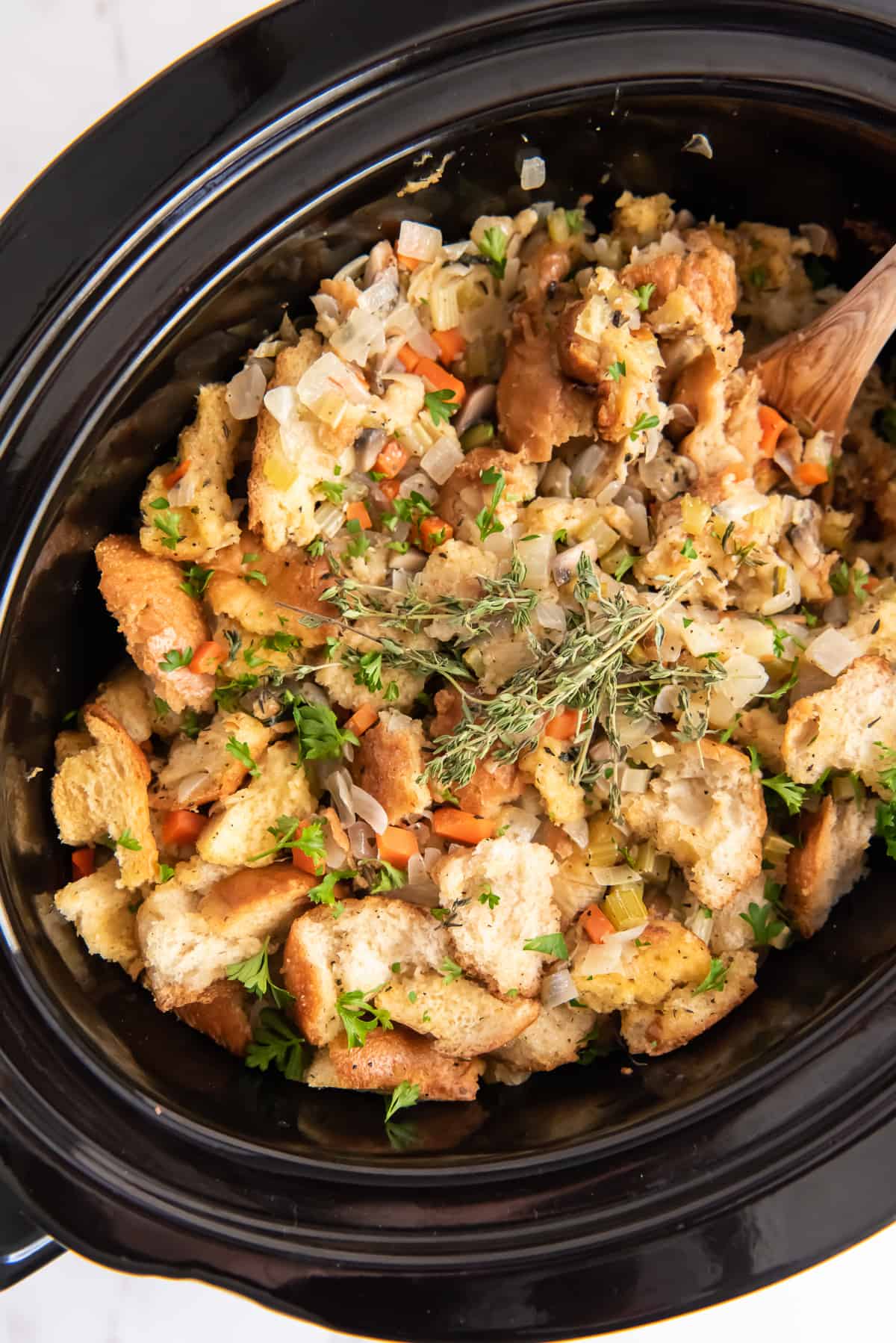 An over the top shot of stuffing in a slow cooker with a wooden spoon.