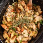 An over the top shot of stuffing in a Crock Pot with a wooden spoon.