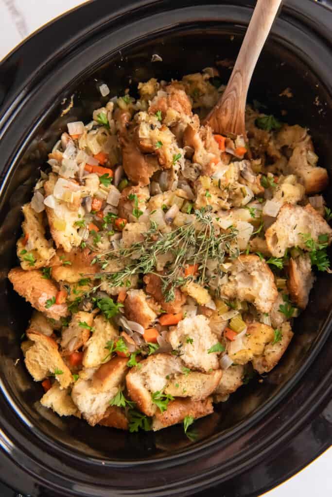 An over the top shot of stuffing in a Crock Pot with a wooden spoon.