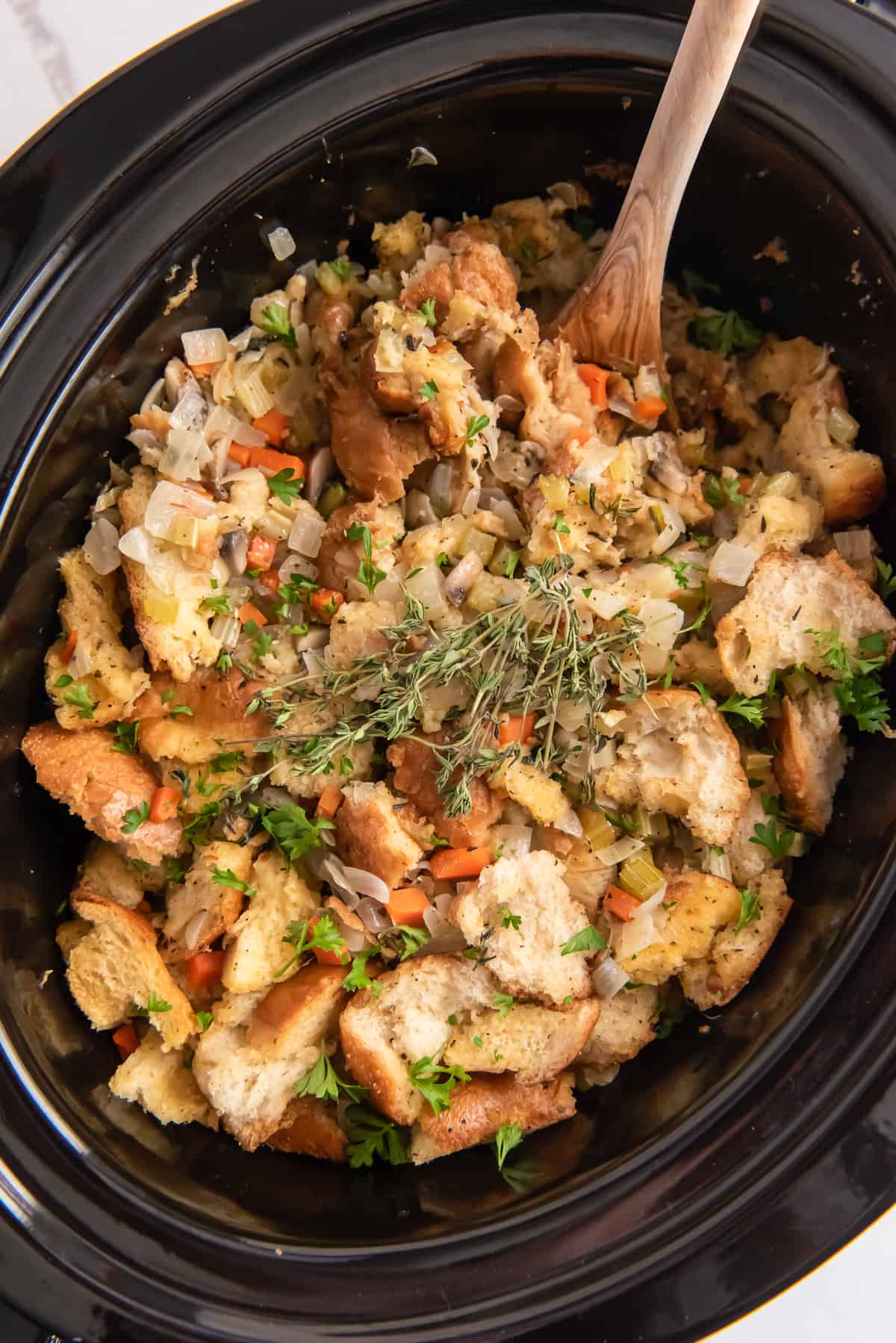 An over the top shot of stuffing in a Crock Pot with a wooden spoon.