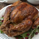 A golden brown turkey on a platter with bay leaves.