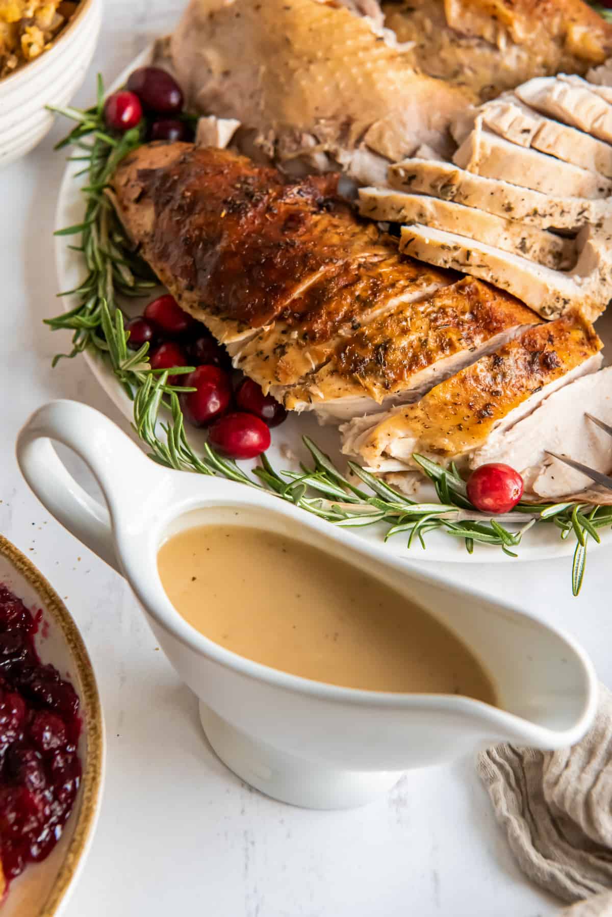 A gravy boat next to a platter of turkey.