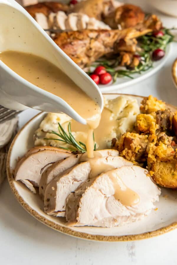 Turkey gravy pouring from a gravy boat over slices of turkey on a dinner plate.