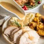 Gravy pouring from a gravy boat over sliced turkey on a plate.