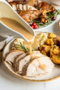 Gravy pouring from a gravy boat over sliced turkey on a plate.