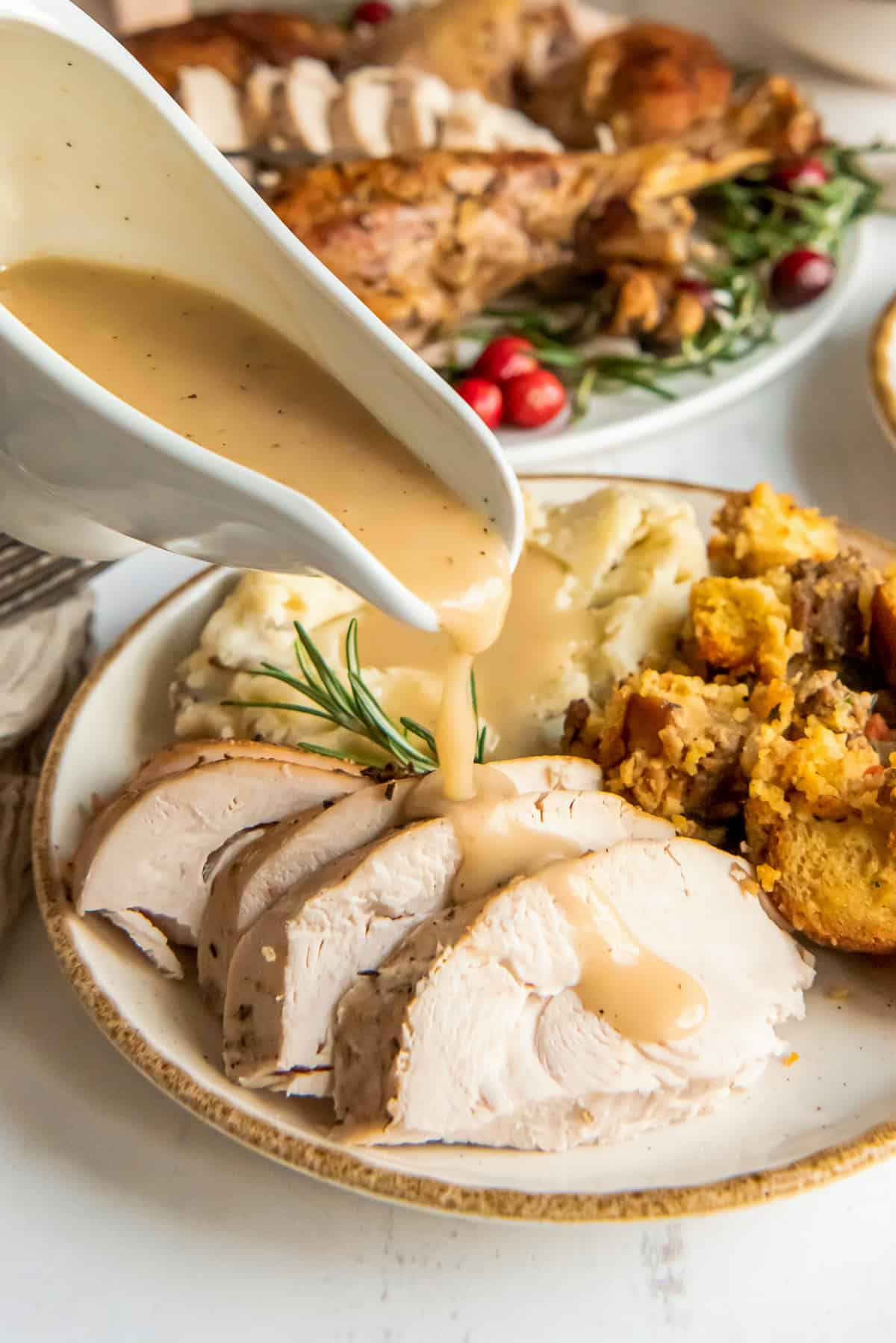 Gravy pouring from a gravy boat over sliced turkey on a plate.
