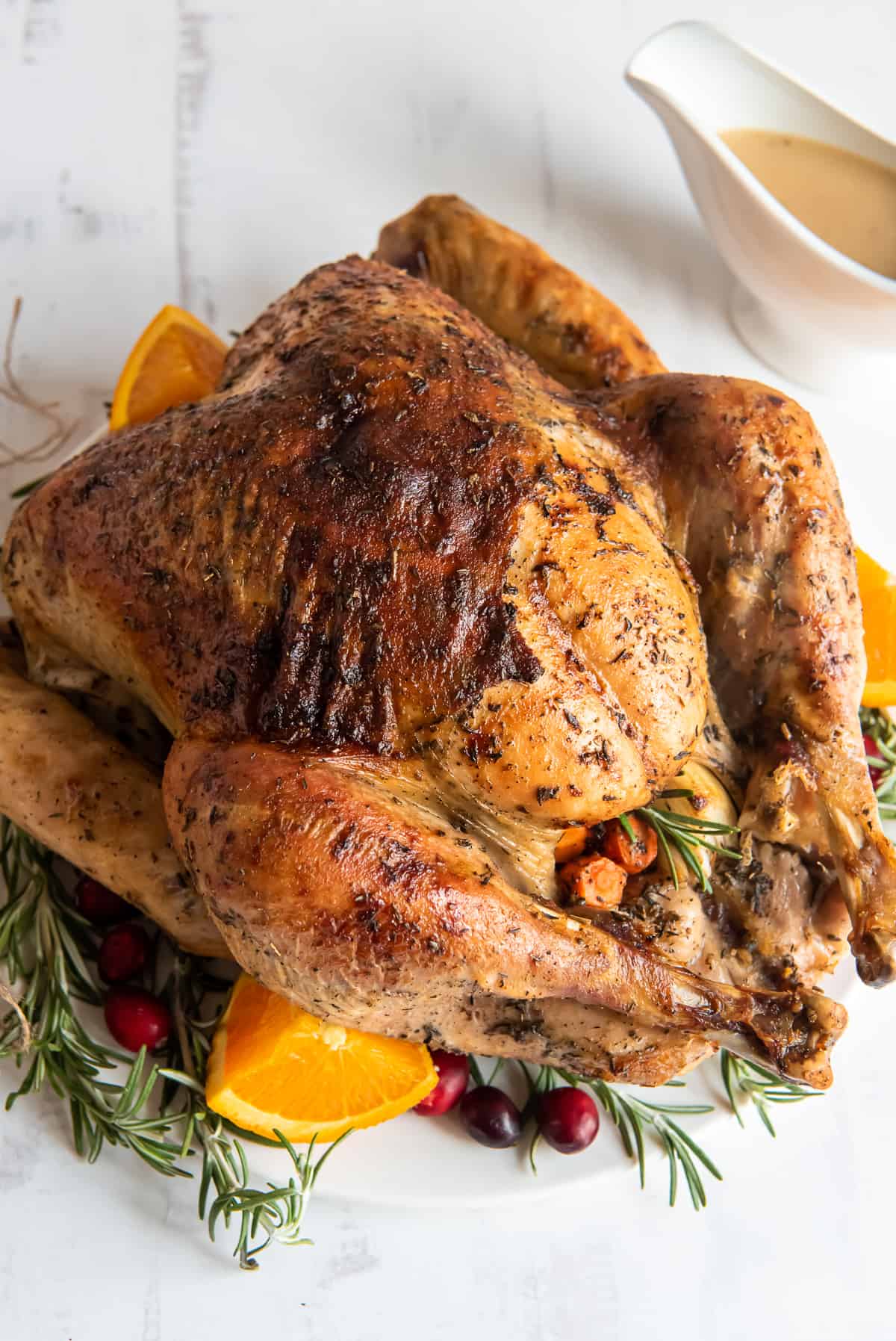 A roasted turkey on a platter with fresh herbs and orange.