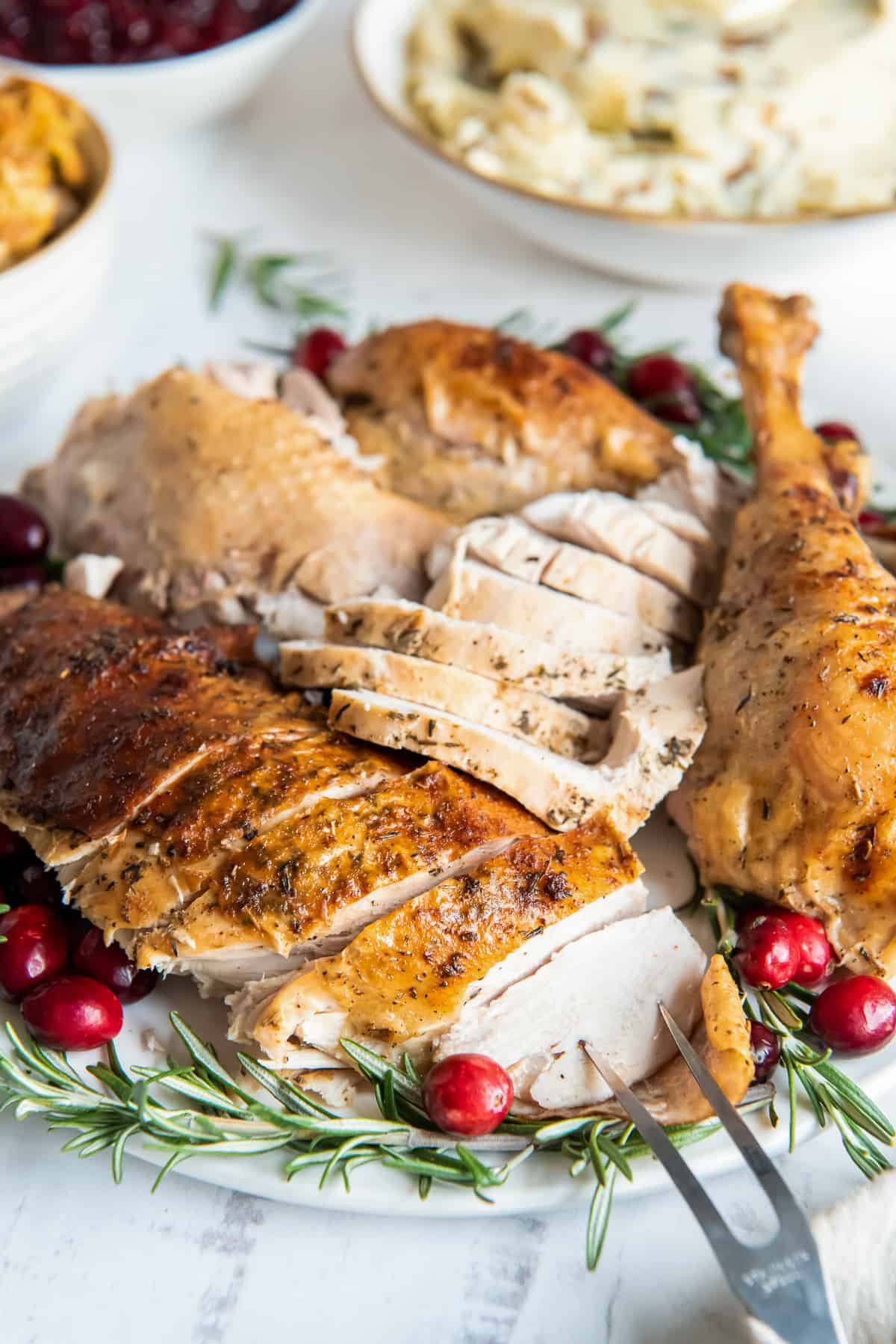 Sliced turkey on a platter with herbs and cranberries.