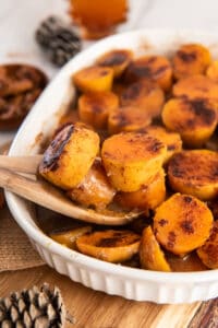 A wooden spoon scoops sweet potatoes from a baking dish.