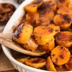 A wooden spoon scoops sweet potatoes from a baking dish.