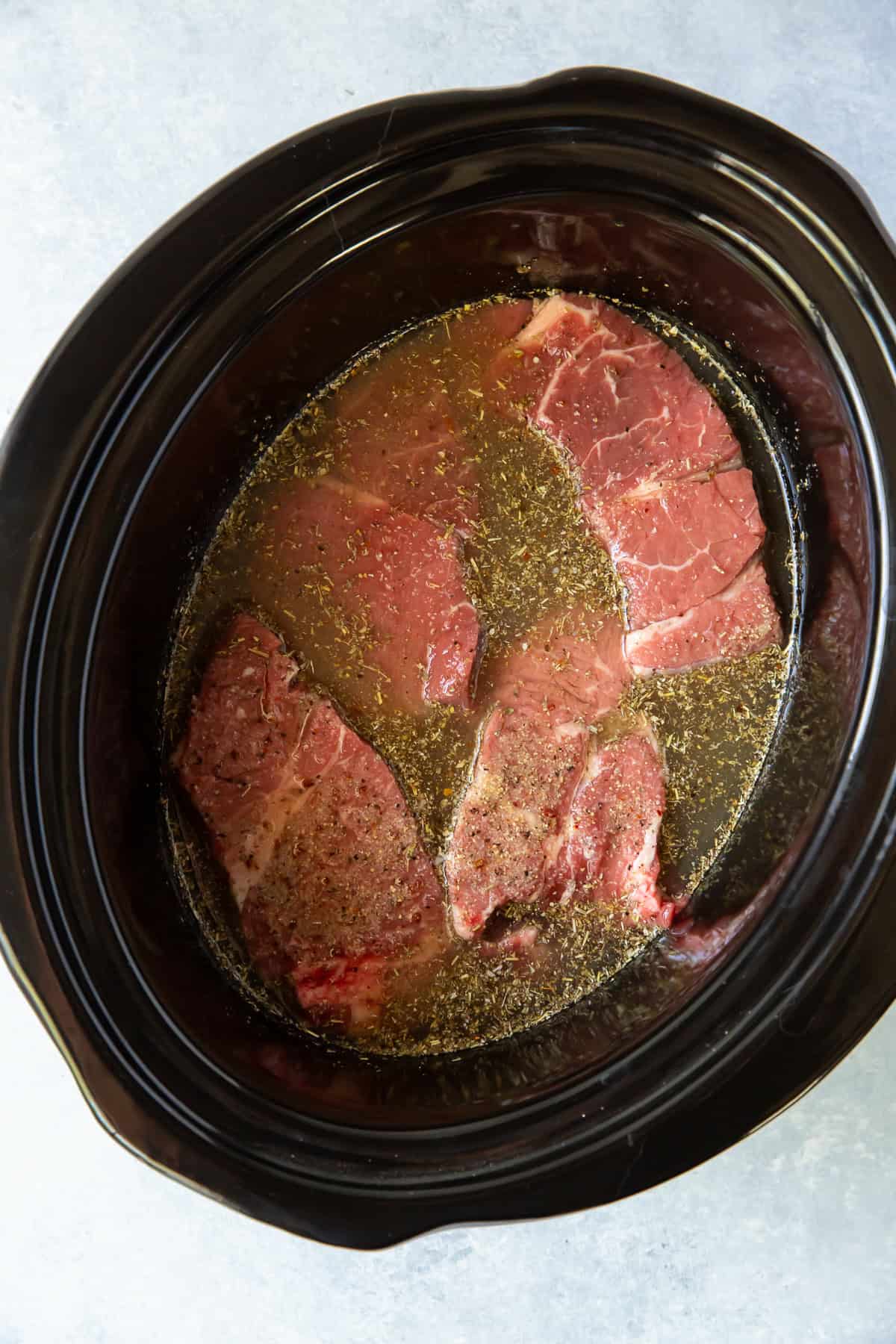 Broth added to a slow cooker insert with chunks of chuck roast.