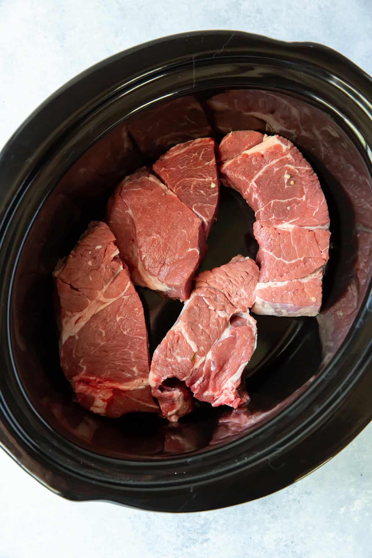 Big chunks of chuck roast in a slow cooker insert.