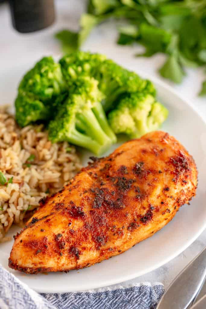 A close up of a seasoned air fryer chicken breast on a plate with broccoli and rice.